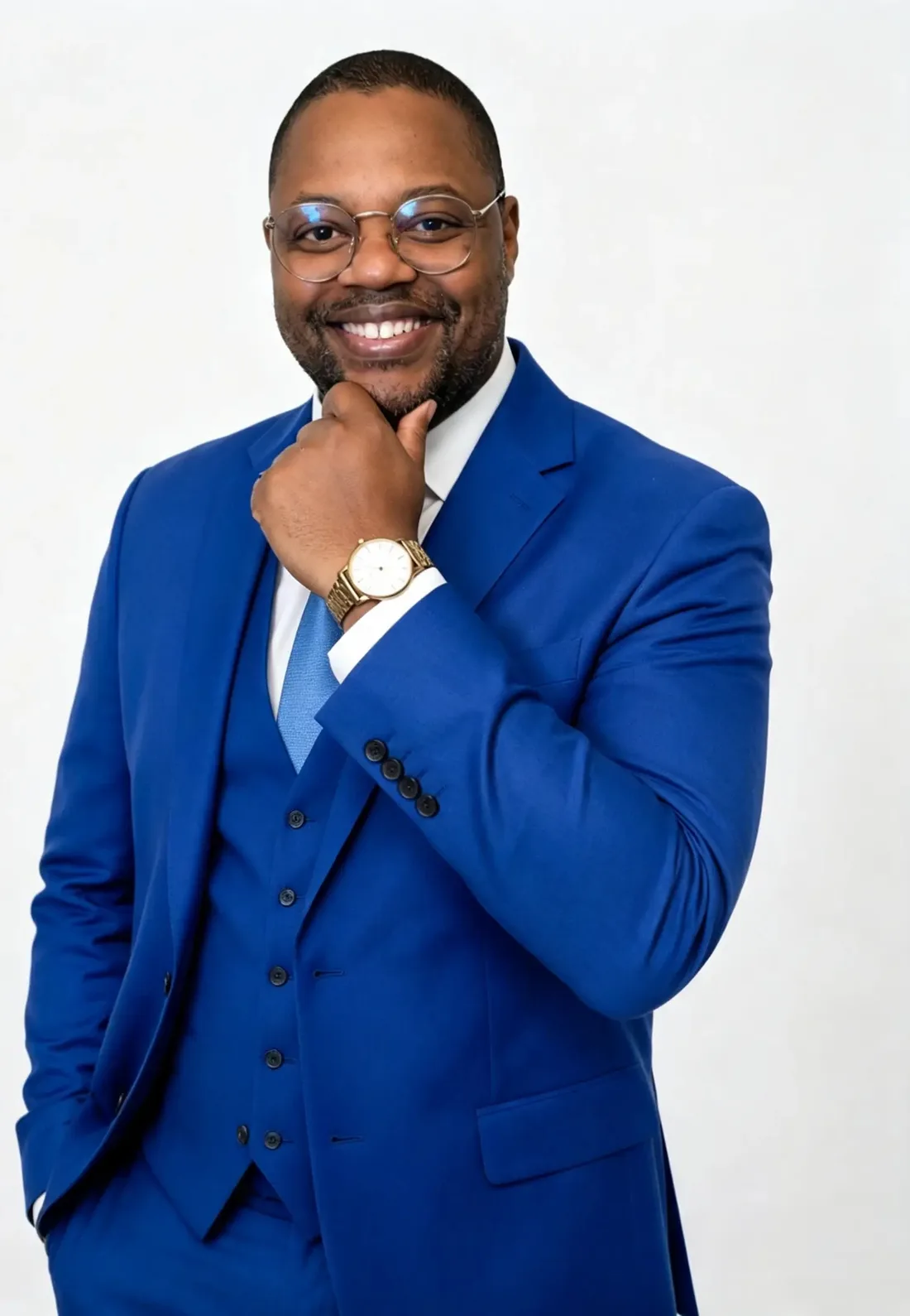 Yossef Leandro, de terno azul royal e gravata azul, sorrindo com a mão apoiada no queixo